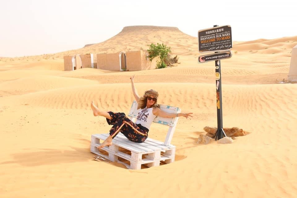 Frau auf Bank vor einem Naturdenkmal und Berg in der Wüste inmitten von Sanddünen