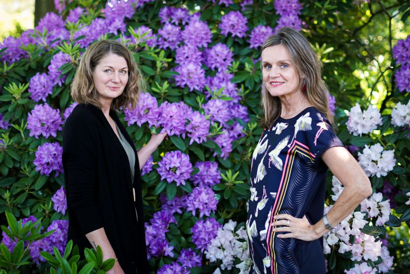 Zwei Frauen stehen vor einem blühenden Rhododendronbusch